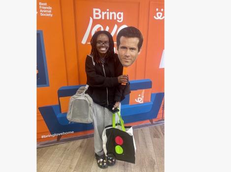 Person holding a Ryan Reynolds face on a stick with the cat carrier holding the cat she'd adopted
