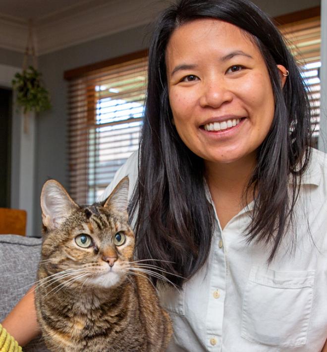 Smiling person sitting on a couch with a cat next to them