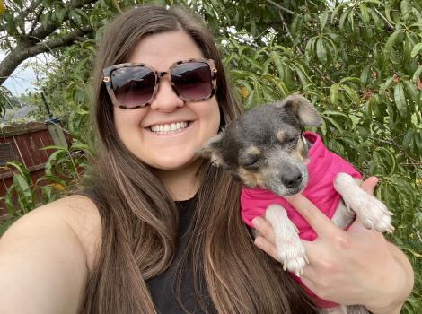 Selfie of Katie holding Berry the dog, who is wearing a pink jacket