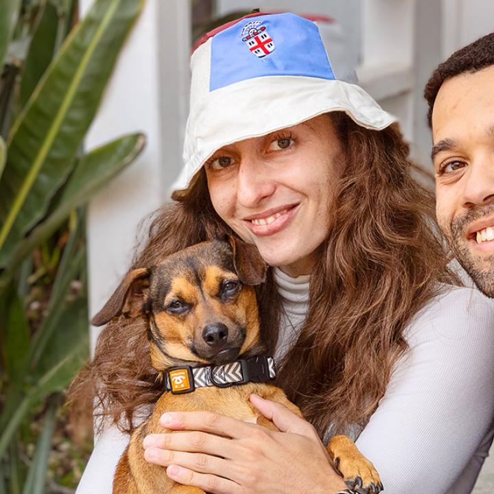 Couple holding a small dog sitting beside some plants