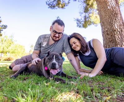 Smiling people relaxing with a dog in the grass under a tree