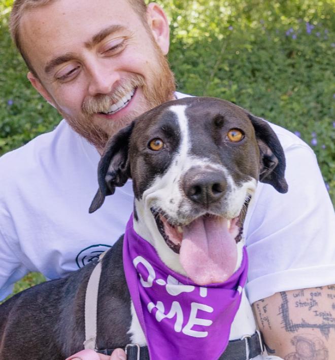 Smiling person kneeling in grass holding a happy dog in their arms