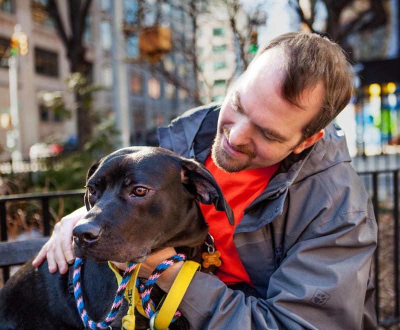 Smiling person sitting in a park in New York City with a dog
