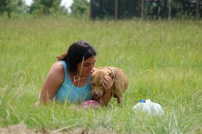 Person sitting in grass cradling a brown dog's head in her hands