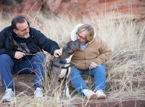 Jessa the dog with her adopters outside in some dried grass