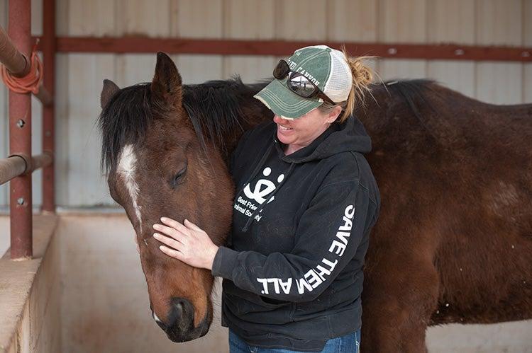 Woman wearing a Best Friends sweatshirt cradling a horse's head in a stall