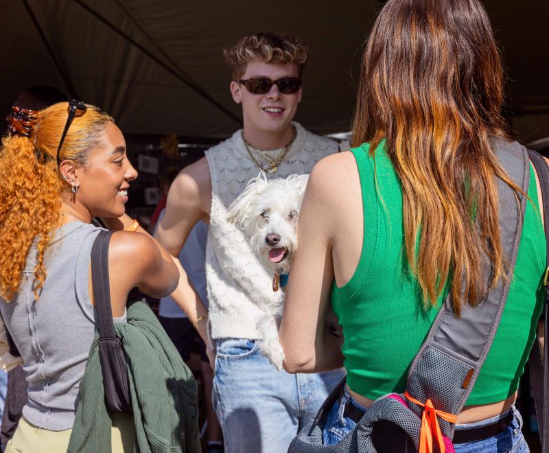 Person holding a small white dog talking to two other people