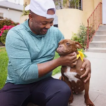 Smiling person sitting with a dog outside on some steps